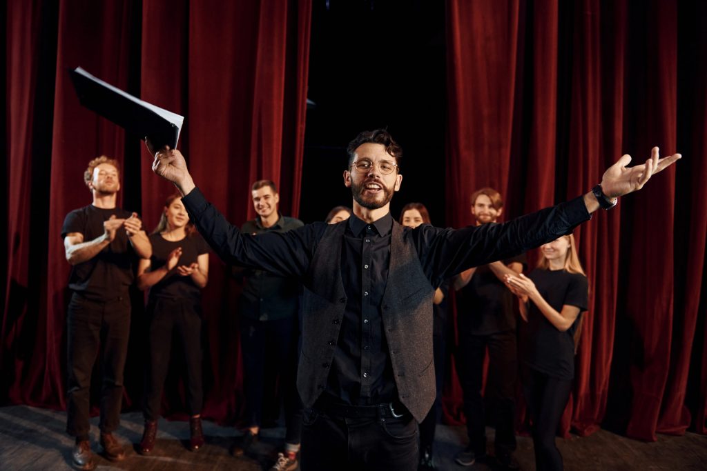 Man is practicing his role. Group of actors in dark colored clothes on rehearsal in the theater