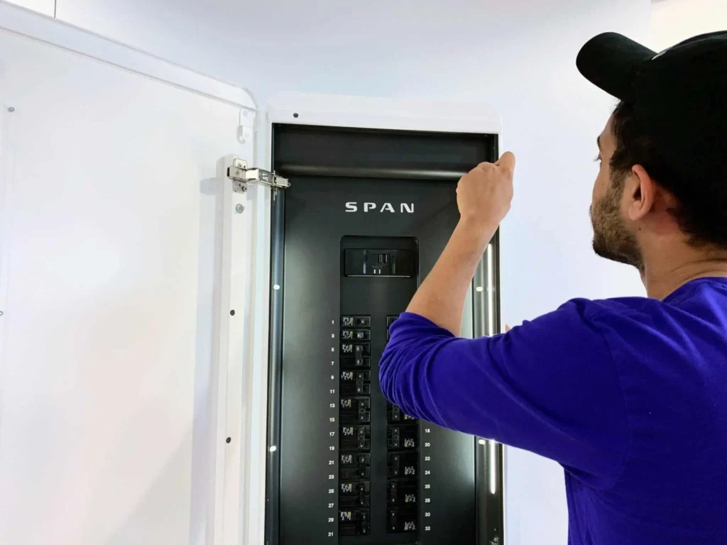 Man adjusting a SPAN electrical panel during installation, showcasing electrical services relevant to indoor air quality and energy efficiency in Kent, WA.